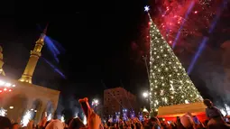 Warga mengambil gambar pohon natal yang sedang dihiasi percikan kembang api di dekat Masjid Mohammad al-Amin di Beirut, Lebanon (10/12). Pohon natal ini dipajang bersebelahan dengan Masjid Mohammad al-Amin. (AFP Photo/Stringer)