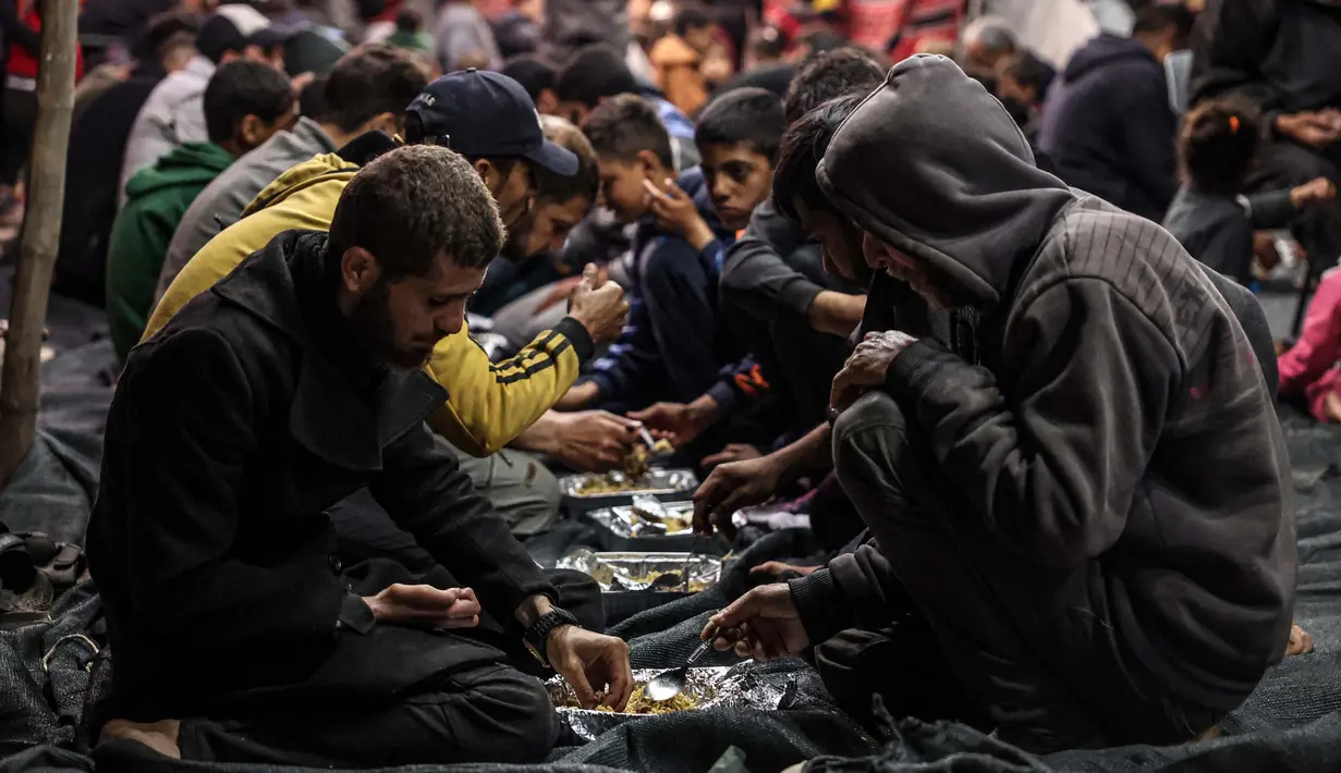 Warga Palestina berbagi makanan berbuka puasa pada hari pertama bulan puasa Ramadan, di sebuah kamp pengungsi di Rafah, Jalur Gaza Selatan pada 11 Maret 2024. (Foto: SAID KHATIB / AFP)