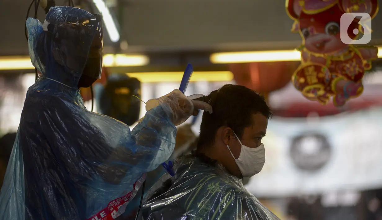 Tukang cukur mengenakan alat pelindung diri (APD) dari plastik saat mencukur rambut pelanggan di Pondok Kelapa, Jakarta, Selasa (5/5/2020). Tukang cukur mengenakan APD untuk mengurangi risiko penularan virus corona COVID-19. (merdeka.com/Imam Buhori)
