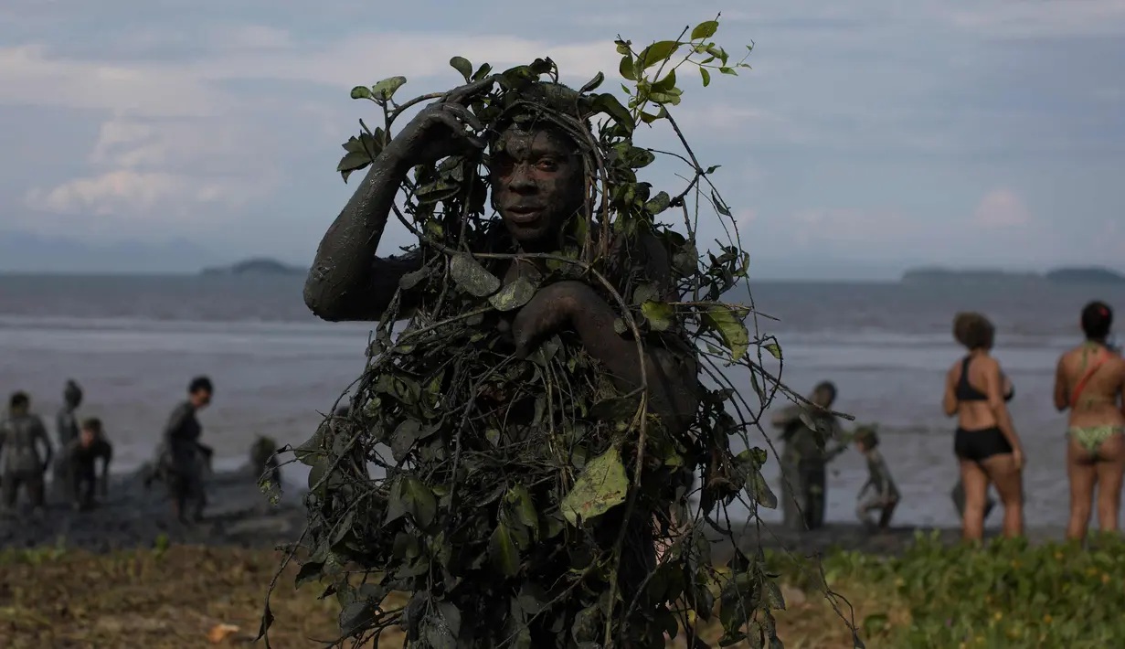 Seorang peserta berpose dengan tumbuhan yang dilumuri lumpur selama pesta karnaval "Bloco da Lama" atau "Lumpur Lumpur" di Paraty, Brasil, (10/2). (AP Photo / Leo Correa)