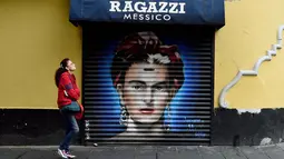 Seorang wanita melintasi mural seniman Frida Kahlo di sebuah jalan wilayah bersejarah Mexico City, Meksiko, 30 Agustus 2017. Mural menjadi salah satu langkah Pemerintah Mexico City untuk melestarikan dan mempercantik ruang publik. (ALFREDO ESTRELLA/AFP)