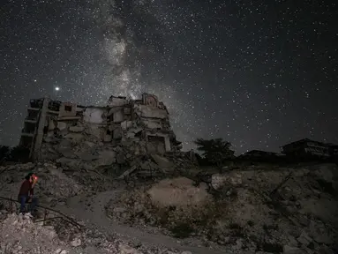 Seorang pria memandangi Galaksi Bima Sakti yang menghiasi langit malam saat dia duduk di antara reruntuhan bangunan akibat pengeboman di Kota Ariha, Provinsi Idlib, Suriah, Sabtu (27/6/2020). (Omar HAJ KADOUR/AFP)
