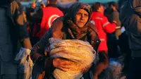Seorang ibu yang dievakuasi membawa bantuan makanan dari lembaga kemanusiaan di kota al-Rasyidin, Suriah (15/12). Ribuan warga telah dievakuasi di kota yang kini porak-poranda. (REUTERS/Ammar Abdullah)