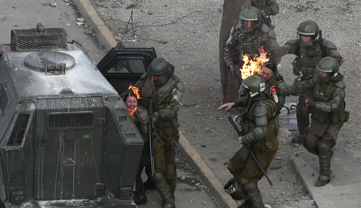 Petugas polisi berlari untuk mendapatkan bantuan setelah dipukul dengan bom bensin yang dilemparkan oleh pengunjuk rasa selama protes anti-pemerintah di Santiago, Chile (4/10/2019). (AP Photo/Esteban Felix)