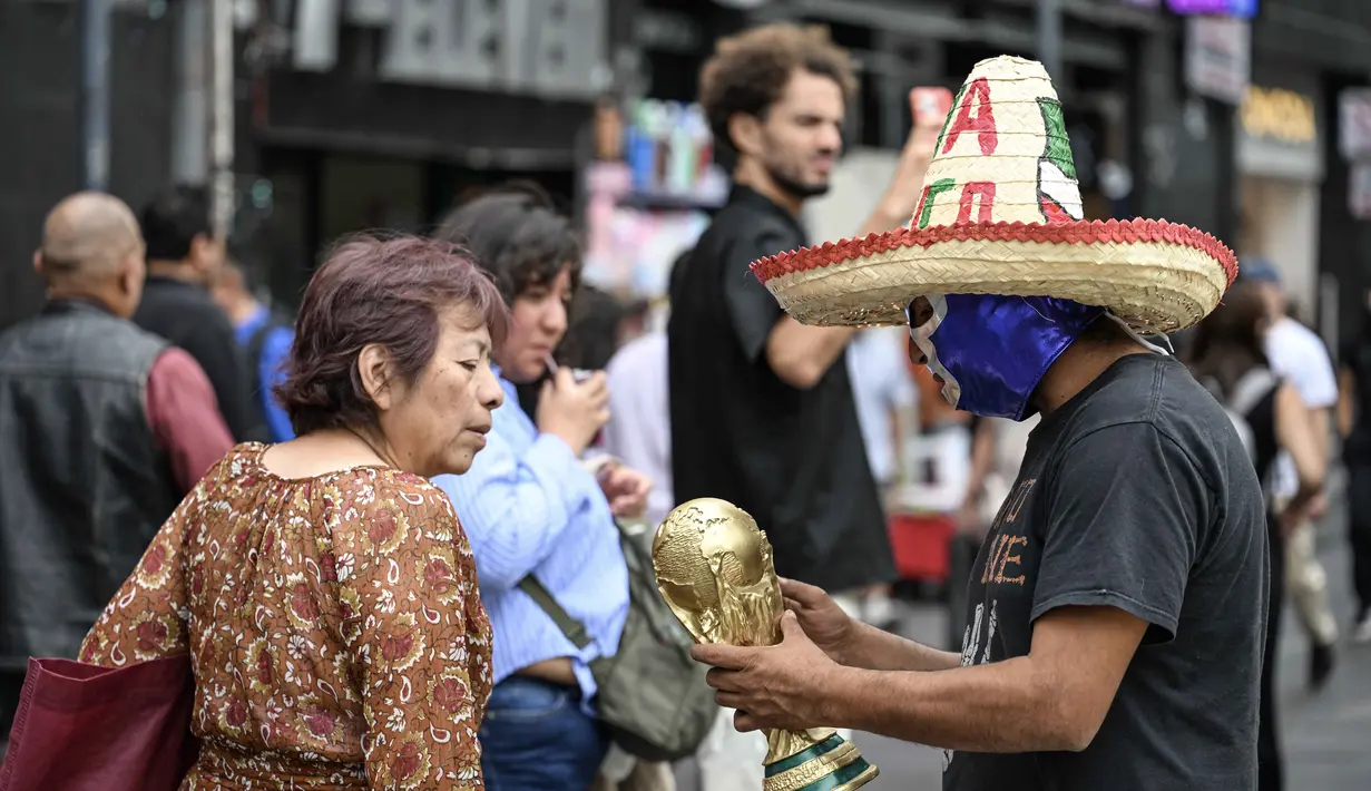 Seorang pedagang kaki lima yang mengenakan topeng gulat tradisional Meksiko menunjukkan suvenir berbentuk piala Piala Dunia kepada pejalan kaki di Mexico City, Senin 8 Juni 2026. (Yuri CORTEZ/AFP)