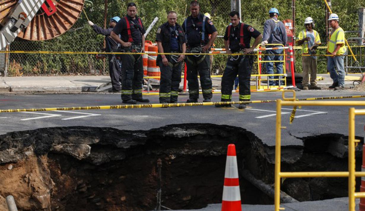 Petugas pemadam kebakaran mengamati  lubang besar (sinkhole) di wilayah Brooklyn, New York, Selasa (4/8/2015). Lubang yang terbentuk di persimpangan pemukiman Sunset Park itu disebabkan erosi dan merusak pipa air serta aspal jalan. (AFP/Kena Betancur)