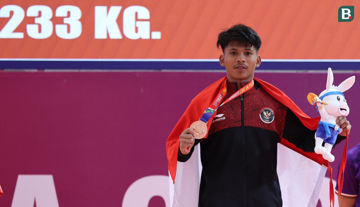 Atlet angkat besi Indonesia, Muhammad Husni berpose memegang medali perunggu nomor angkat besi putra 55 kg SEA Games 2023 di Taekwondo Hall Olympic Complex, Phnom Penh, Kamboja, Sabtu (13/05/2023). Husni berhasil melakukan total angkatan 233 kg, dengan rincian 133 kg snatch dan 120 clean & jerk. (Bola.com/Abdul Aziz)