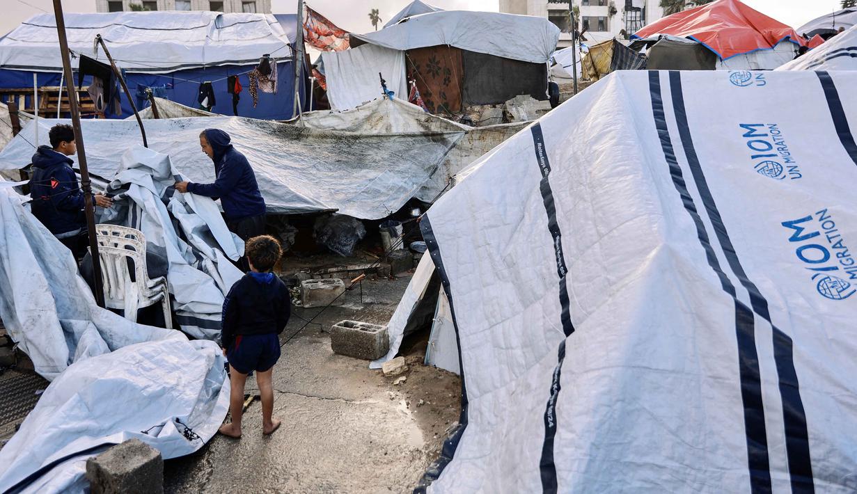 Pemerintah Gaza telah menyatakan kebutuhan mendesak akan sekitar 200.000 unit rumah prefabrikasi (rakitan) untuk menampung para pengungsi yang kehilangan tempat tinggal. Tampak dalam foto, seorang pria dan pemuda Palestina yang mengungsi menyesuaikan terpal tenda keluarga mereka saat wilayah tersebut dilanda hujan dan kondisi musim dingin yang dingin, di Kota Gaza pada 28 Desember 2025. (Omar AL-QATTAA/AFP)