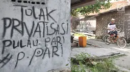 Wisatawan bersepeda melintasi coretan protes di salah satu tembok rumah di Pulau Pari, Kepulauan Seribu, Jakarta, Minggu (29/4). Coretan dibuat warga yang menolak klaim PT Bumi Pari Asri atas kepemilikan lahan Pulau Pari. (Merdeka.com/Iqbal S. Nugroho)