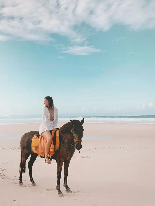 Berhasil memotret keindahan pantai dan langit yang luar biasa, Pamela Bowie berpose di atas kuda dengan robe dan celana pendek putih. Foto: Instagram.