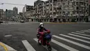 Seorang wanita mengendarai skuter di jalan yang sepi di distrik Yangpu, di Shanghai (28/3/2022). Jutaan orang di pusat keuangan China dikurung di rumah mereka pada Maret 28 ketika bagian timur Shanghai dikunci untuk mengekang wabah Covid terbesar di negara itu. (AFP/Hector Retamal)