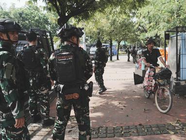 Seorang penjual minuman bersepeda melintas di depan personel Tentara Nasional Indonesia (TNI) yang berjaga di sebuah jalan setelah beberapa hari terjadi aksi unjuk rasa menentang kenaikan tunjangan anggota Dewan Perwakilan Rakyat (DPR), di Jakarta, Senin 1 September 2025. (AP Photo/Tatan Syuflana)
