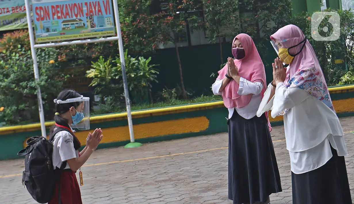Seorang murid memberi salam kepada guru saat memasuki sekolah  SD Negeri 6, Bekasi, Jawa Barat, Selasa (4/8/2020). Pemerintah setempat memberikan izin kepada enam sekolah untuk melakukan uji coba pembelajaran tatap muka selama satu bulan. (Liputan6.com/Herman Zakharia)