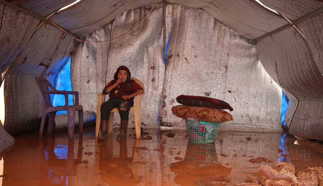Seorang anak duduk dalam tendanya yang kebanjiran di Kamp Cordoba, Batabu, Idlib, Suriah, Rabu (16/1). Hujan badai membuat kamp pengungsian mereka kebanjiran. (Aaref Watad/AFP)