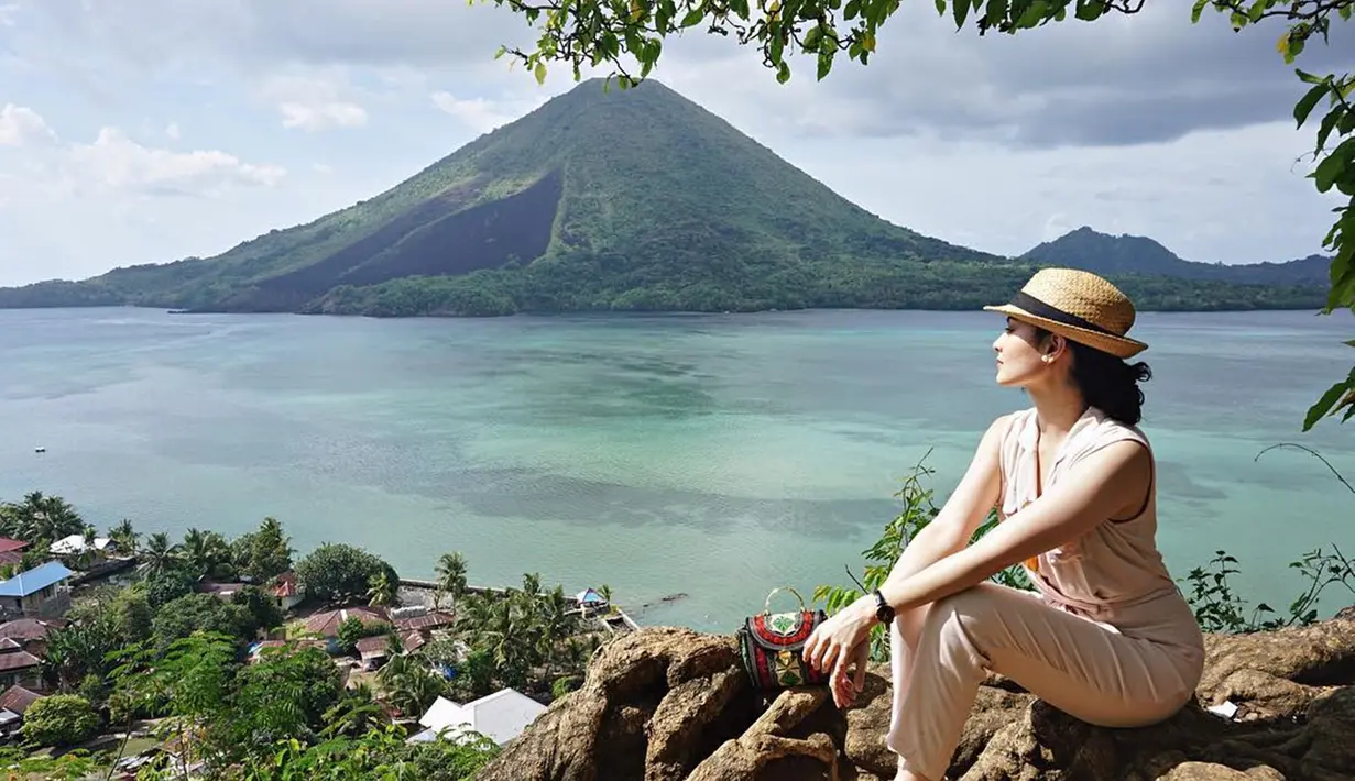 Posenya di sebuah bebatuan dengan latar belakang gunung dan pantai di Banda Besar sangat menakjubkan. Menggunakan pakaian serba krem ditambah dengan aksesoris topi jerami dan jam tangan hitam, membuatnya tampak semakin mempesona. (Liputan6.com/IG/clarabernadeth)