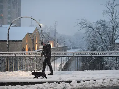 Seorang wanita berjalan-jalan dengan seekor anjing di tengah salju di Milan, Italia (28/12/2020). Hujan salju mengguyur Milan pada Senin (28/12). (Xinhua/Daniele Mascolo)