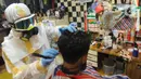 Seorang tukang cukur mengenakan alat pelindung diri (APD) saat memangkas rambut pelanggannya di Chemot Barbershop, Ciawi, Bogor, Jawa Barat, Minggu (5/4/2020). Penggunaan APD tersebut sebagai antisipasi agar lebih waspada terhadap penularan virus corona Covid-19. (merdeka.com/Arie Basuki)