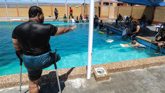 Majdi al-al-Tatar (kiri), instruktur renang saat melatih pemuda Palestina yang diamputasi di sebuah kolam renang di Kota Gaza (30/7/2019). Tatar melatih warga Palestina yang diamputasi untuk membantu mereka mempertahankan aktivitas fisik. (AFP Photo/Mahmud Hams)