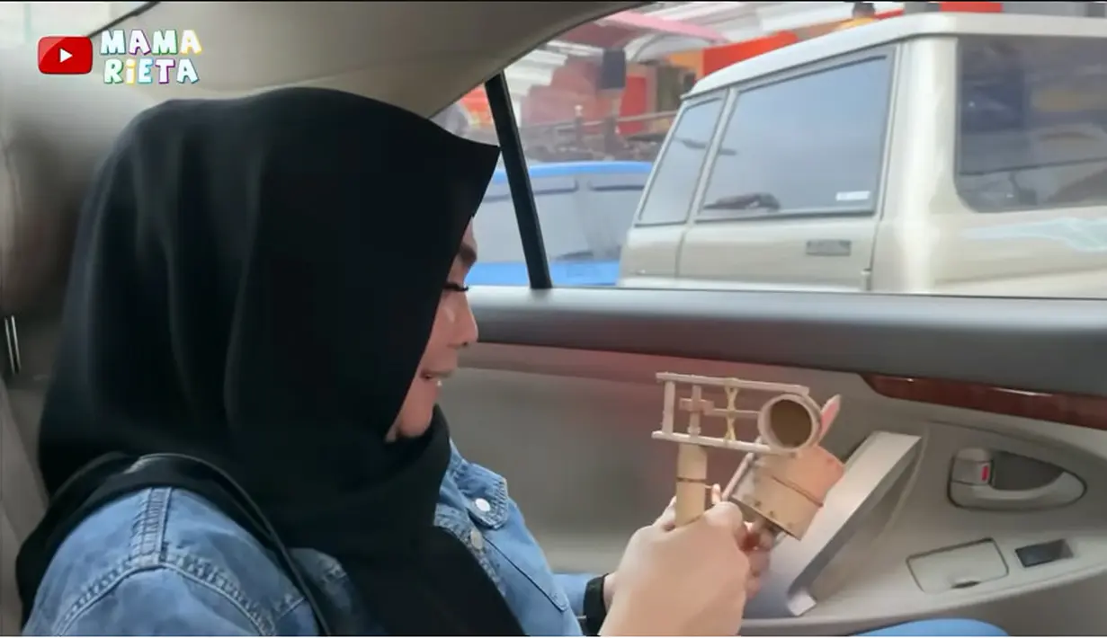Hari itu juga, selesai meeting Mama Rieta mencari makan gudeg. Sebelumnya, ia terlebih dulu membeli mainan oleh-oleh buat cucunya, Rayyanza alias Cipung. Mama Rieta memegang dua mainan untuk Cipung. [Youtube/Mama Rieta]