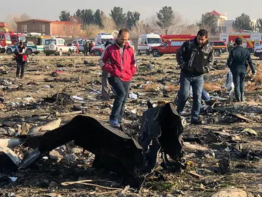 Orang-orang berjalan di antara puing-puing setelah pesawat Boeing 737 jatuh di dekat Bandara Internasional, Teheran, Iran, Rabu (8/1/2020). Seluruh penumpang pesawat maskapai Ukraina yang membawa 176 orang termasuk kru tersebut dilaporkan tewas. (AFP Photo)