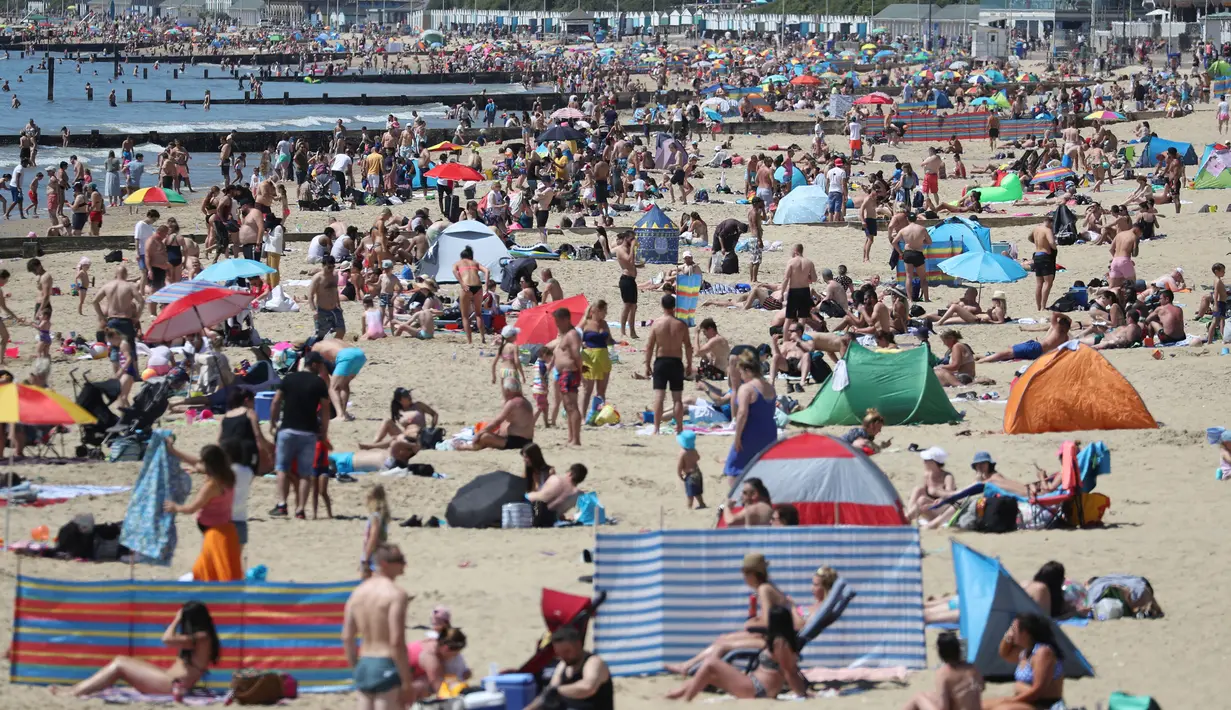 Orang-orang mencoba untuk melakukan jaga jarak ketika berjemur menikmati cuaca panas di pantai pada hari libur umum di Bournemouth, Senin (25/5/2020). Inggris mulai melonggarkan beberapa pembatasan yang diberlakukan untuk mengendalikan penyebaran virus corona Covid-19. (Andrew Matthews / PA via AP)