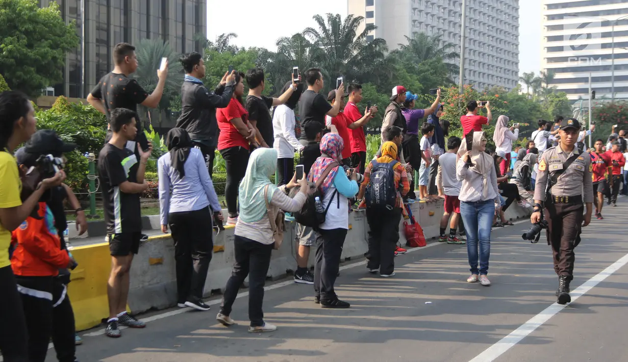 Warga yang tengah mengikuti Car Free Day (CFD) mengabadikan gambar Parade Asian Games 2018 2018 di Jalan Thamrin, Jakarta, Minggu (13/5). Tak merasa terganggu, mereka justru ikut antusias menyaksikan parade itu. (Liputan6.com/Arya Manggala)