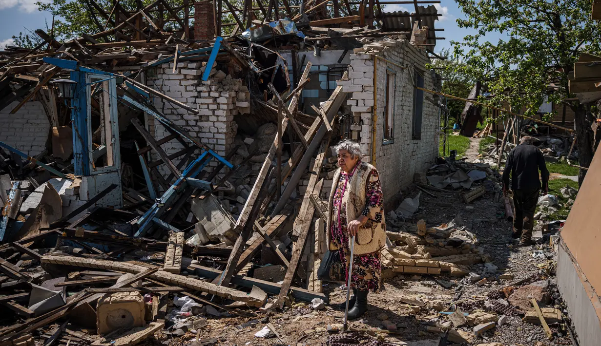 Sepasang penduduk membawa barang bawaan dari rumah mereka yang hancur di tengah invasi Rusia ke Ukraina, di desa Vilkhivka, dekat kota timur Kharkiv, pada 14 Mei 2022. Puluhan rumah di Vilkhivka, sebuah desa berpenduduk sekitar 2.000 jiwa, hancur oleh peluru, ledakan atau kebakaran. Puing-puing berserakan di jalan-jalan termasuk selongsong peluru, dan sisa-sisa amunisi. (Dimitar DILKOFF / AFP)