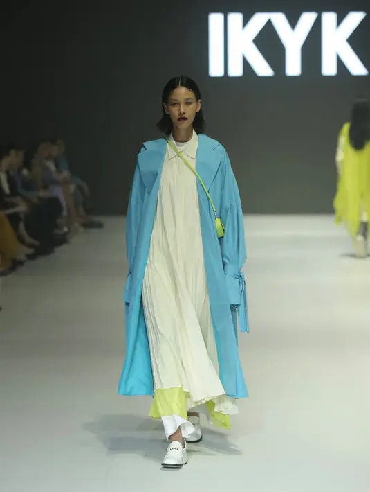 Dress plisket panjang berkerah warna putih, dipadukan dengan coat biru sebagai luaran. Serasi dengan celana panjangnya.  [Fimela/Daniel Kampua]