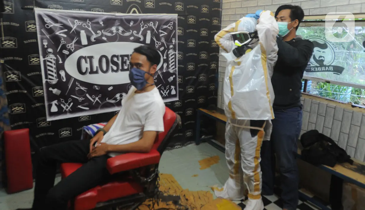 Seorang tukang cukur memakai alat pelindung diri (APD) buatannya sendiri sebelum mencukur pelanggannya di Chemot Barbershop, Ciawi, Bogor, Jawa Barat, Minggu (5/4/2020). (merdeka.com/Arie Basuki)