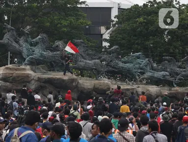 Massa aksi demo tolak omnibus law UU Cipta Kerja naik ke atas patung arjuna wiwaha mengibarkan bendera merah putih di Jalan Medan Merdeka Barat, Jakarta Pusat, Selasa (20/10/2020). Mereka sempat mengibarkan bendera selama kurang lebih lima menit di atas patung. (Liputan6.com/Herman Zakharia)