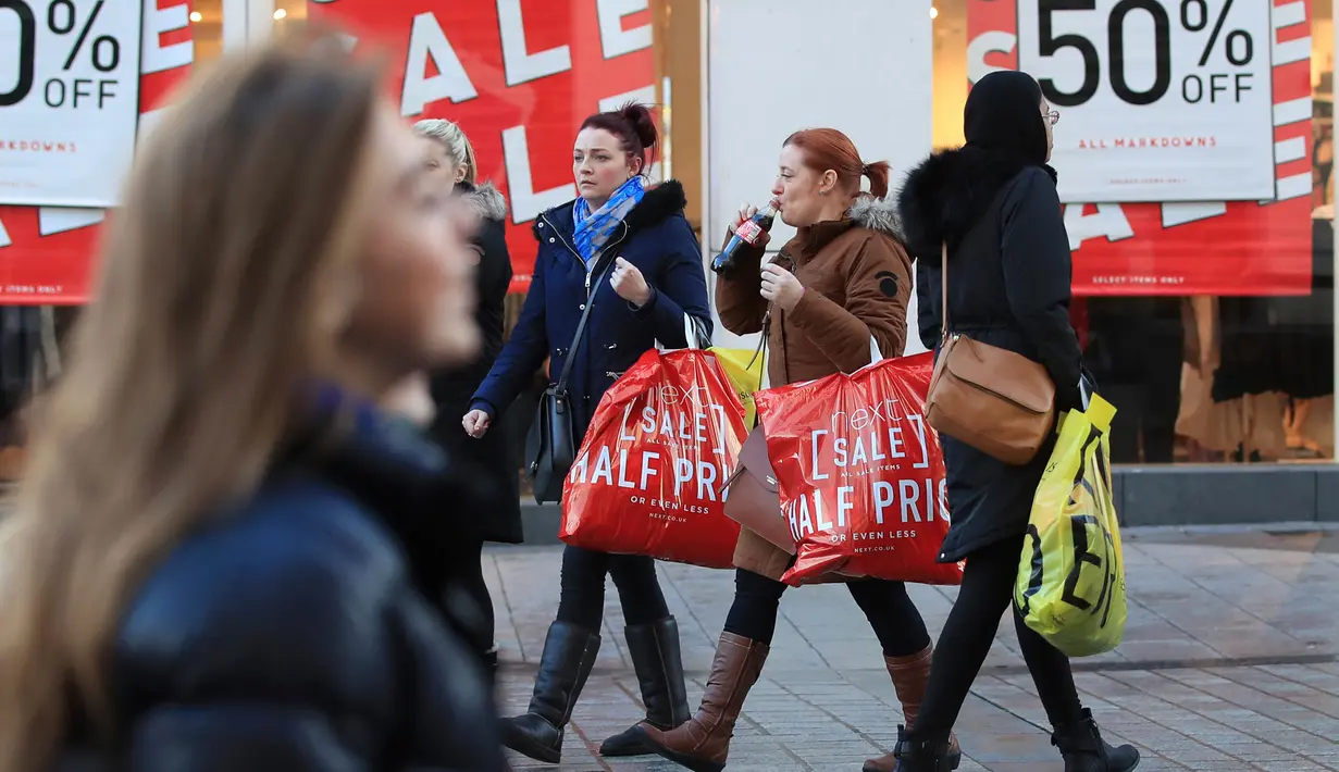 Dua wanita berjalan membawa kantong belanjaan selama Boxing Day di Liverpool, Inggris, Selasa (26/12). Pada Boxing Day, hampir semua pusat pertokoan yang memberikan pesta diskon diserbu para pembeli dan terjadi antrean panjang. (Peter Byrne/PA via AP)