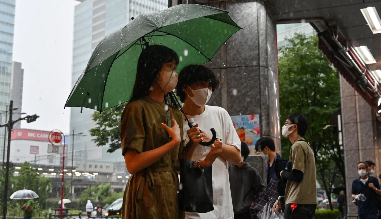 Orang-orang mencari berlindung dari hujan lebat yang terisolasi di distrik Akihabara Tokyo (13/8/2022). Hujan lebat yang dibawa oleh Badai Tropis Meari melanda daerah tersebut. (AFP/ Richard A. Brooks)