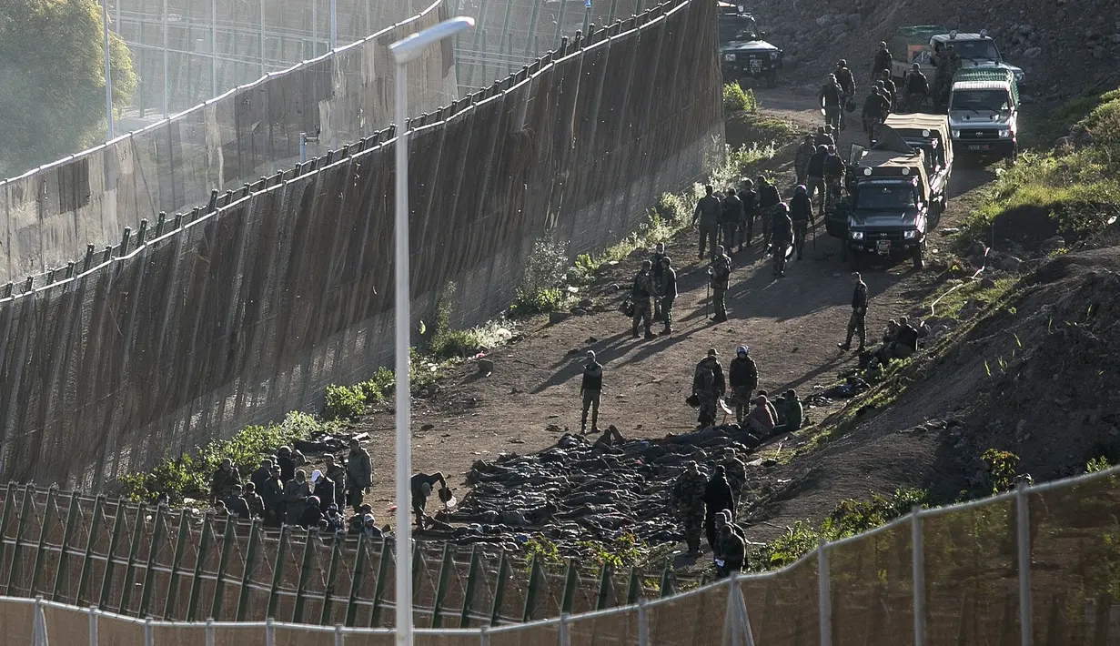 Pasukan keamanan di sisi perbatasan Maroko memaksa para migran untuk berbaring di depan pagar setelah menghentikan mereka melintasi pagar yang memisahkan kantong Spanyol Melilla dari Maroko, di Melilla, Spanyol  (3/3/2022). (AP Photo/Javier Bernardo)