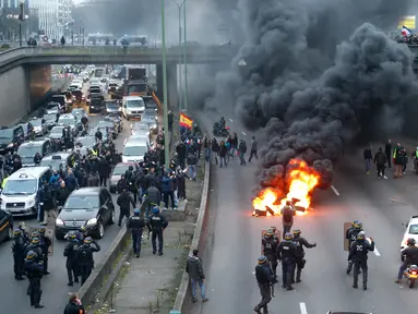 Polisi anti huru-hara tiba ketika pengemudi taksi memblokir jalan dengan membakar ban saat unjuk rasa menentang layanan transportasi VTC seperti Uber, di jalan lingkar di porte Maillot di Paris, Perancis, Selasa (26/1). (AFP PHOTO/Thomas SAMSON)