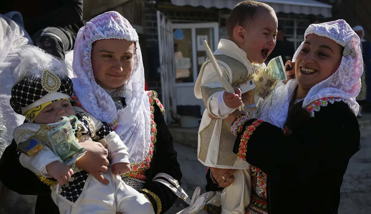 Wanita muslim Bulgaria menggendong putra mereka selama upacara sunat massal untuk anak laki-laki di Desa Ribnovo, 11 April 2021. Penduduk Desa Ribnovo adalah muslim berbahasa Bulgaria, kadang-kadang disebut sebagai "Pomaks" atau "orang yang menderita". (Nikolay DOYCHINOV/AFP)