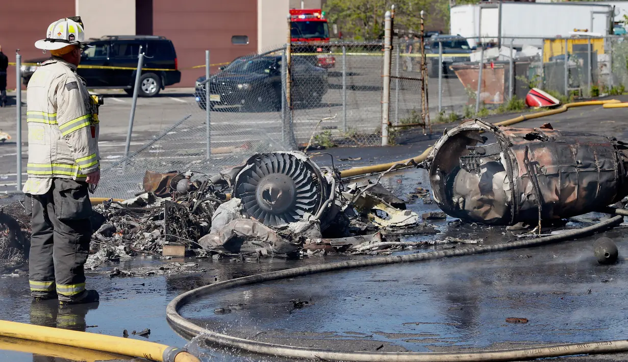 Petugas pemadam mengamati puing pesawat kecil yang jatuh di dekat Bandara Teterboro di luar Kota New York, Senin (15/5). Pesawat itu langsung terbakar setelah menabrak sebuah gedung di komplek bisnis. (Aristide Economopoulos/NJ Advance Media via AP)
