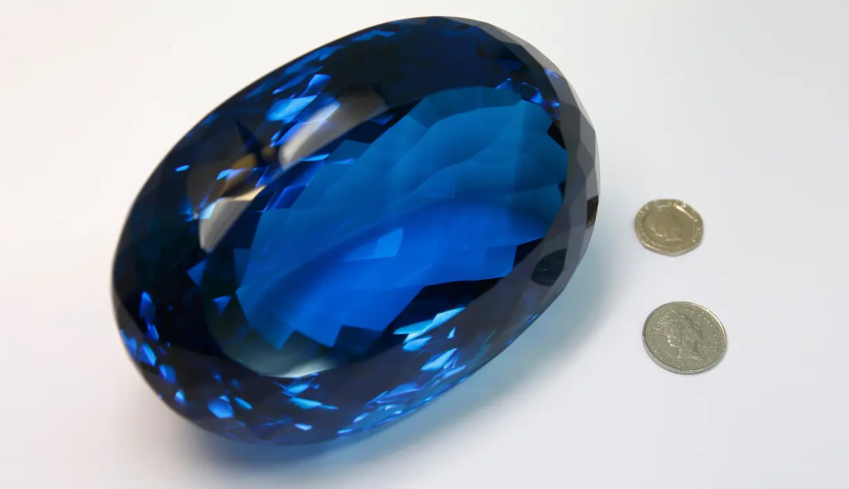 Batu permata jenis topaz berwarna biru disandingkan dengan uang koin di Museum Sejarah Alam London, Inggris, Selasa (27/9). Batu milik Maurice Ostro ini menjadi batu topaz terbesar di dunia. (REUTERS / Peter Nicholls)