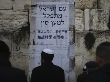 Orang-orang Yahudi berdiri di depan poster dalam bahasa Ibrani dan Tiongkok mengatakan, "Bangsa Israel berdoa untuk China." saat berdoa di Tembok Ratapan, situs paling suci di Kota Tua Yerusalem, Minggu, (16/2/2020). (AP Photo/Ariel Schalit)