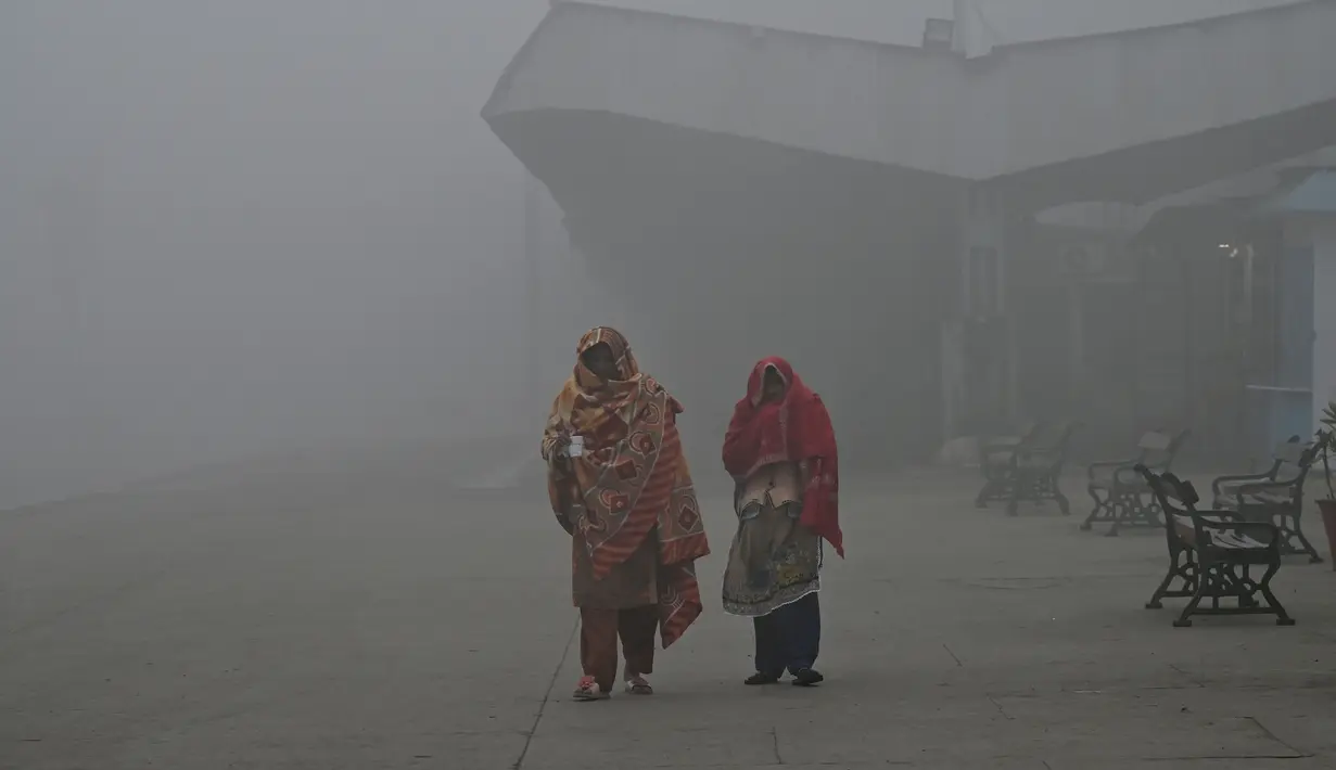 Perempuan berjalan di stasiun kereta api di tengah cuaca berkabut di Lahore (21/12/2022). Beberapa penerbangan dialihkan ke bandara lain akibat cuaca berkabut. (AFP/Arif Ali)
