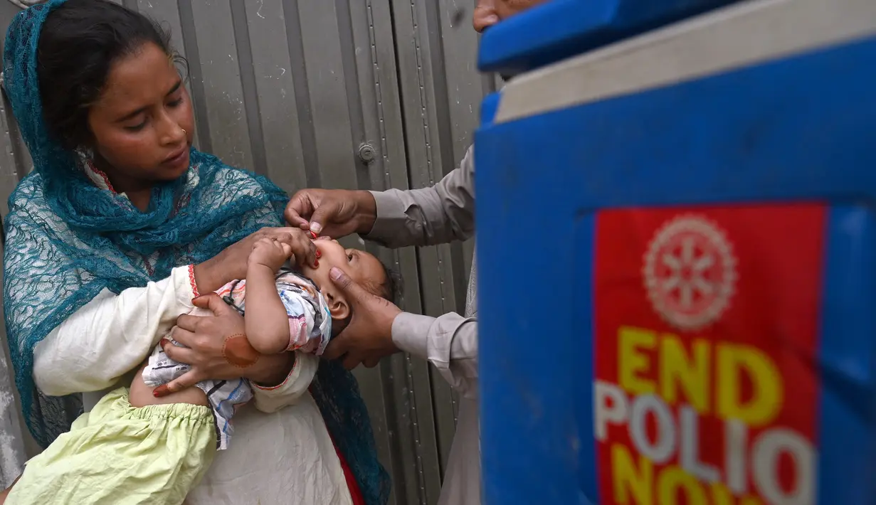 Seorang petugas kesehatan memberikan tetes vaksin polio kepada seorang anak saat kampanye vaksinasi polio dari rumah ke rumah di sebuah kawasan kumuh di Lahore, Paksistan, Senin (23/5/2022). Pakistan meluncurkan upaya anti-polio baru pada hari Senin, lebih dari seminggu setelah pejabat mendeteksi kasus ketiga tahun ini di wilayah barat laut negara itu yang berbatasan dengan Afghanistan. (Arif ALI / AFP)