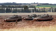 Seorang tentara Israel berjalan melewati tank Merkava yang terparkir di dekat perbatasan dengan Jalur Gaza, Israel, Senin (6/5/2019). Para pemimpin Palestina di Gaza menyetujui gencatan senjata dengan Israel. (JACK GUEZ/AFP)