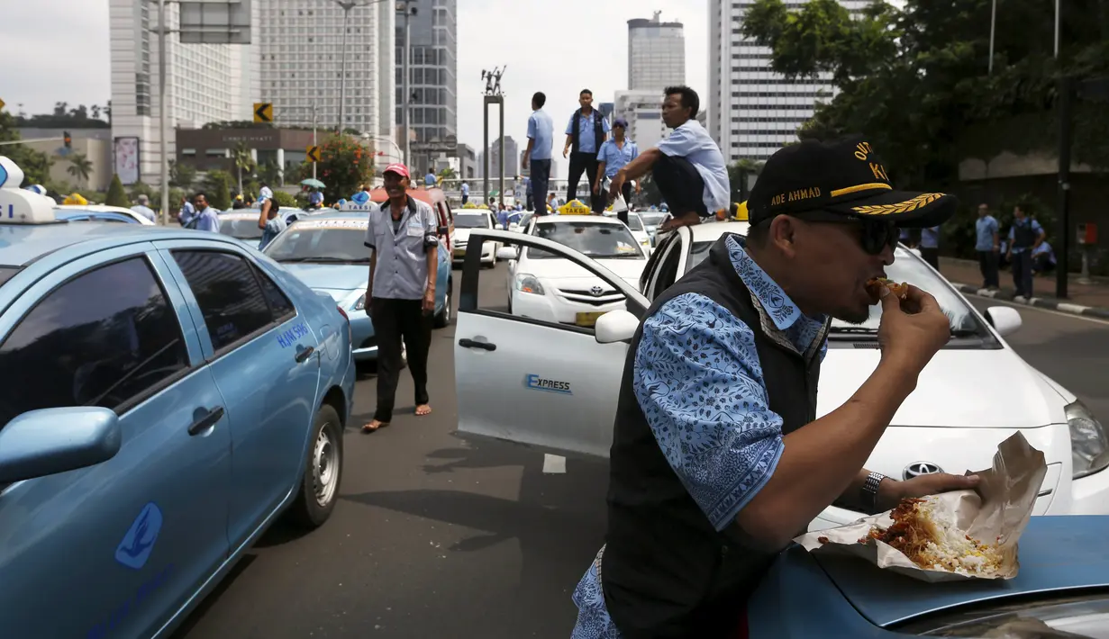 Seorang sopir taksi saat makan siang selama aksi protes terhadap aplikasi transportasi di Jakarta, Selasa (22/3). Ribuan Sopir taksi turun ke jalan. Mereka berdemonstrasi menolak keberadaan angkutan online berpelat hitam. (REUTERS/Beawiharta)