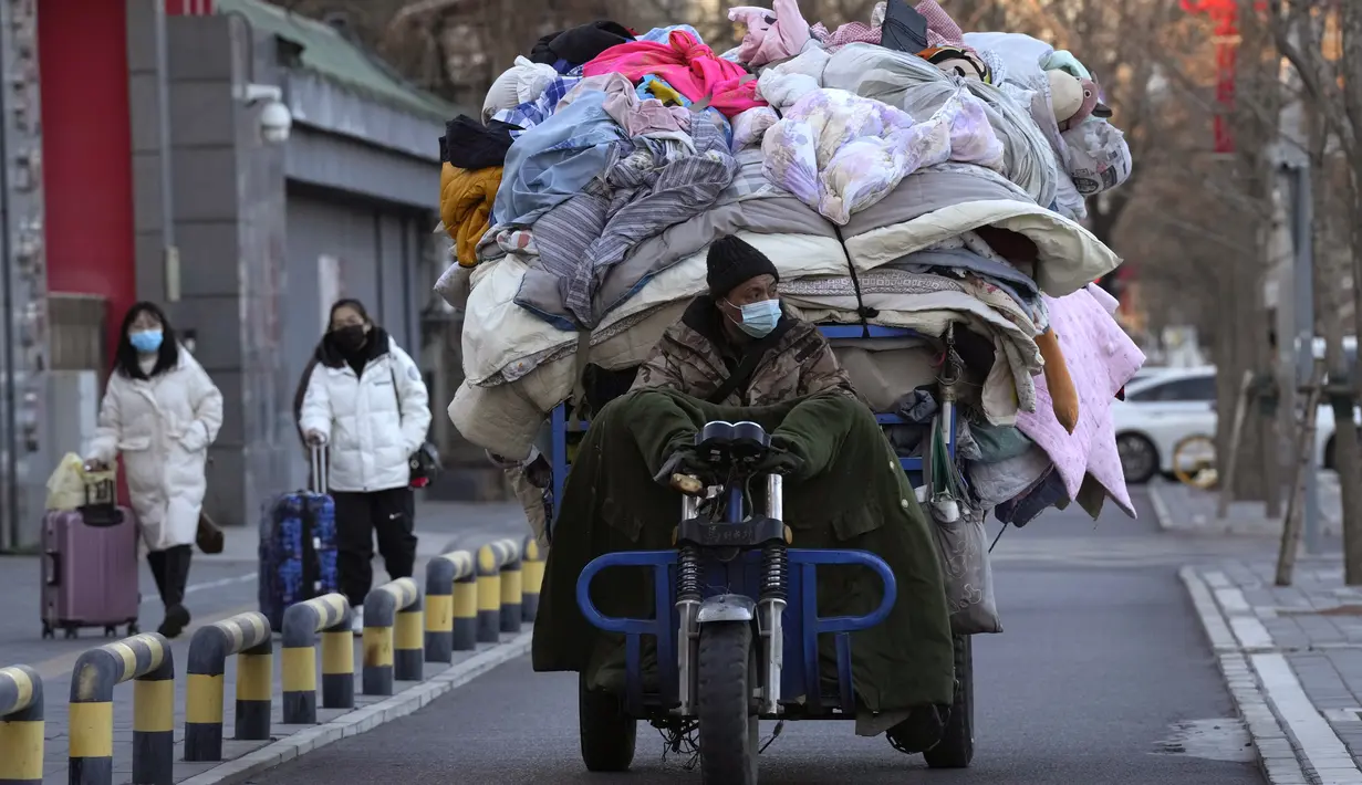Seorang pria bertopeng mengangkut selimut bekas dan bahan kain lainnya di Beijing, Jumat, 30 Desember 2022. Strategi "nol-Covid" mengurung jutaan keluarga di rumah mereka selama berminggu-minggu, menutup sebagian besar perjalanan masuk dan keluar China, dan mengosongkan jalan-jalan ramai di kota-kota besar. (AP Photo/Ng Han Guan)