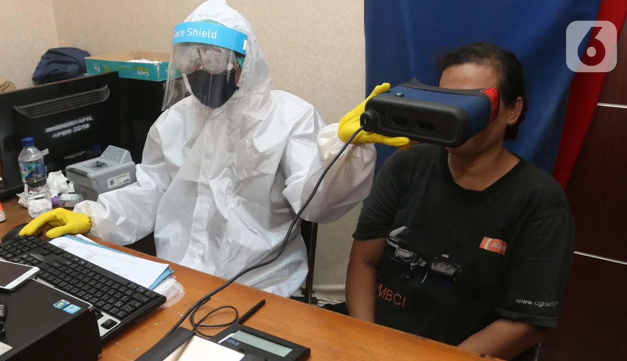 Petugas menggunakan Alat Pelindung Diri (APD) saat merekam mata warga yang mengajukan pembuatan KTP Elektronik di Pondok Aren, Tangerang Selatan, Senin (15/6/2020). Penggunaan APD ini bertujuan meminimalisir kontak fisik sebagai upaya pencegahan penularan Corona COVID-19. (Liputan6.com/Angga Yuniar)