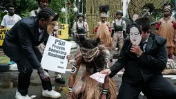 Mereka menyuarakan kritik terhadap ancaman deforestasi besar-besaran untuk Proyek Strategis Nasional (PSN) tebu di Merauke. Tampak dalam foto, aktivis Greenpeace Indonesia bersama beberapa pemuda Papua menggelar aksi teatrikal saat berunjuk rasa di depan Kantor Kementerian Koordinator bidang Perekonomian, Jakarta, Kamis (18/12/2025). (Yasuyoshi Chiba/AFP)
