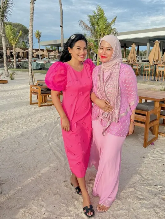 Berada di pantai, Titik mengenakan dress panjang pink fuschia yang dihiasi beberapa beads. Lengan model balon, dipadukan sandal Hermes hitam. [@titi_kamall]