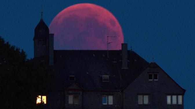 Bulan tampak berwarna merah darah saat terjadinya fenomena gerhana bulan total  di Bernkastel-Kues, Jerman, Jumat (27/7). Gerhana bulan yang terlama pada abad ini dapat disaksikan di seluruh dunia dengan mata telanjang. (Harald Tittel/dpa via AP)