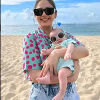 Jessica Mila terlihat chic bahkan saat menggendong sang anak di pantai. Ia tampil kasual mengenakan kaus bercorak abstrak berwarna semarak dan celana jeans. Kyarra, sang putri juga tampil gemas dengan baju bayi berwarna biru muda pastel, dipakaikan sunglasses kecil agar serasi dengan sang mama. [Foto: Instagram/jesicamila03]