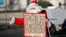 Seorang petualang asal Prancis, Remi Le Calvez membawa poster bertuliskan 'Pole Nord' yang artinya kutub utara, mencari tumpangan kendaraan dengan mengenakan kostum Santa Claus di Paris, Prancis, Selasa (6/12). (Reuters/Benoit Tessier)