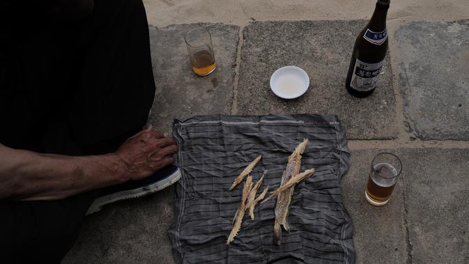 Seorang pria menikmati ikan kering dan bir di pantai Sijung Ho di Korea Utara (14/7/2019). Pantai Sijung Ho merupakan tujuan wisata populer bagi penduduk lokal dan asing. (AP Photo/Vincent Yu)